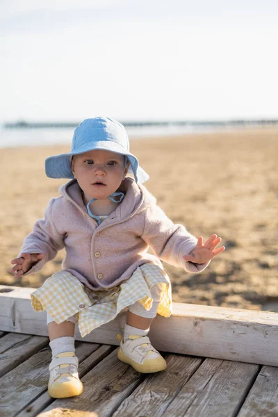 Bébé fille assis sur une jetée en bois sur une plage floue à Trévise — Photo de stock