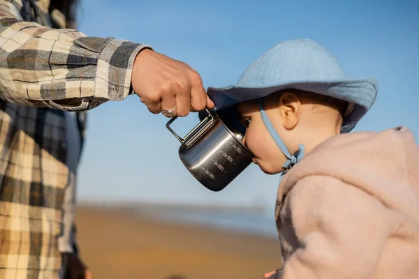 Father holding cup near baby in panama hat on beach — Stock Photo