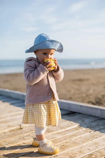 Bambino in cappello panama mangiare mela sul molo di legno a Treviso — Foto stock