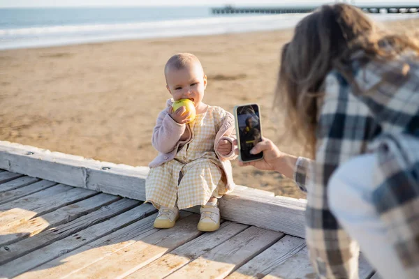 Blurred father taking photo of baby with apple on wooden pier in Italy — Stock Photo