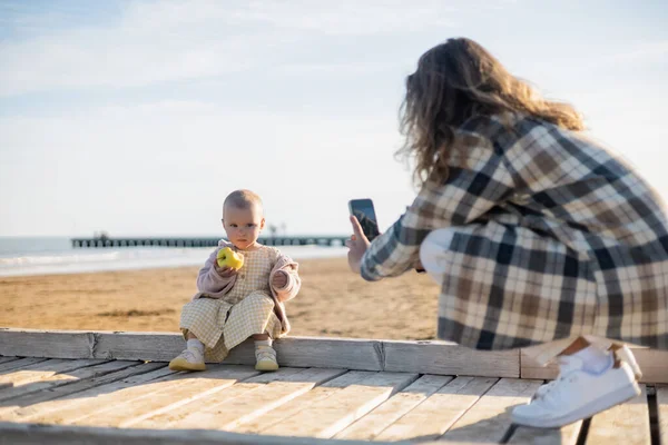 Homme flou prenant une photo de bébé fille avec pomme sur jetée en Italie — Photo de stock