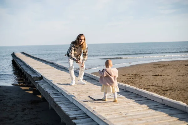 Pai feliz olhando para a filha bebê andando no cais perto do mar em Treviso — Fotografia de Stock