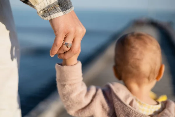 Обратный вид отца, держащего за руку размытую дочку малыша на пирсе — стоковое фото