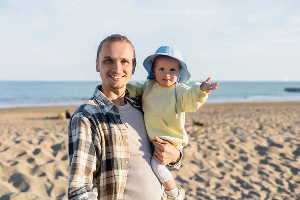 Улыбающийся мужчина смотрит в камеру, держа дочку на пляже в Тревизо — стоковое фото