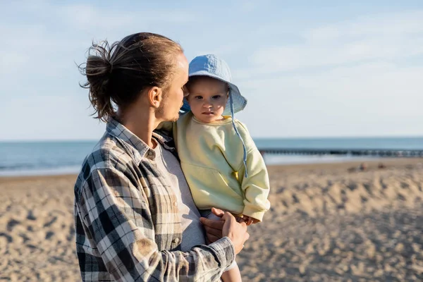 Pai de cabelos compridos olhando para a menina no chapéu de panamá na praia na Itália — Fotografia de Stock