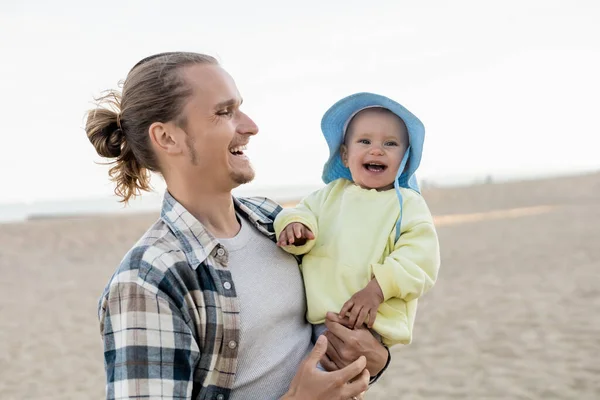 Glücklicher Papa schaut Tochter mit Panamahut am Strand an — Stockfoto