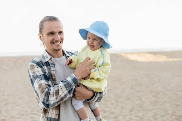 Père positif en chemise jouant avec l'enfant sur la plage — Photo de stock