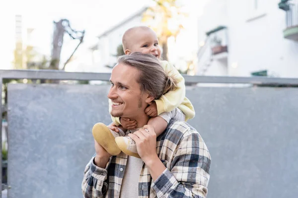Smiling baby sitting on shoulders of young father on urban street in Treviso — Stock Photo