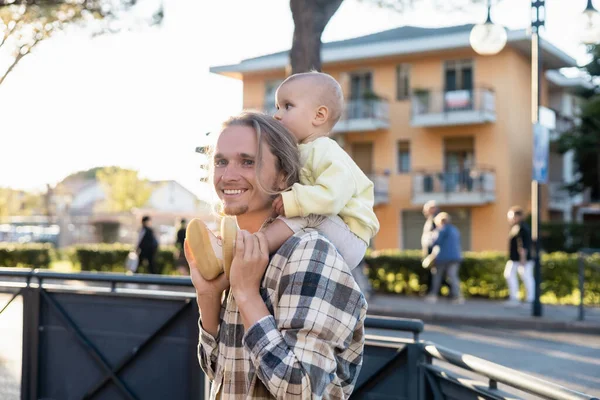 Счастливый молодой человек с ребенком на плечах на городской улице в Тревизо — стоковое фото
