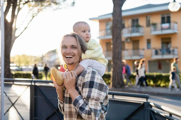 Cheerful young man carrying baby on shoulders on urban street in Treviso — Stock Photo