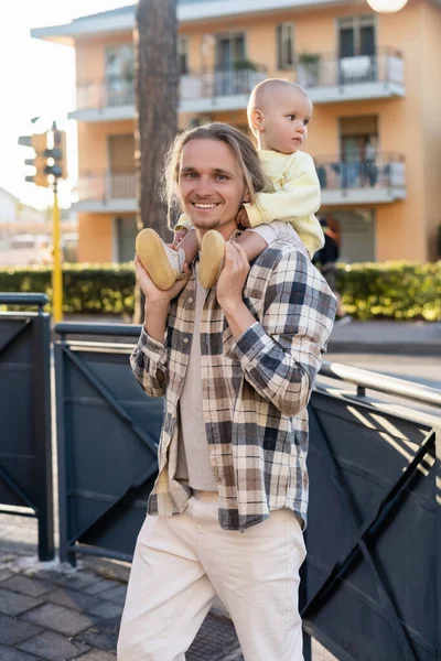 Smiling man carrying baby on shoulders and looking at camera on urban street in Treviso — Stock Photo