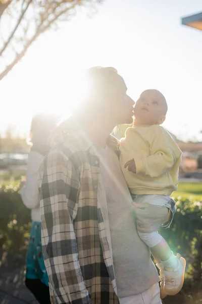 Jeune homme embrassant bébé fille contre la lumière du soleil en plein air à Trévise — Photo de stock