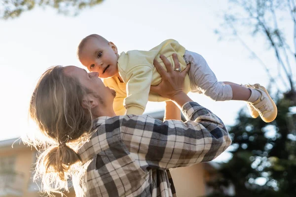 Low angle view of young man playing with baby outdoors — Stock Photo