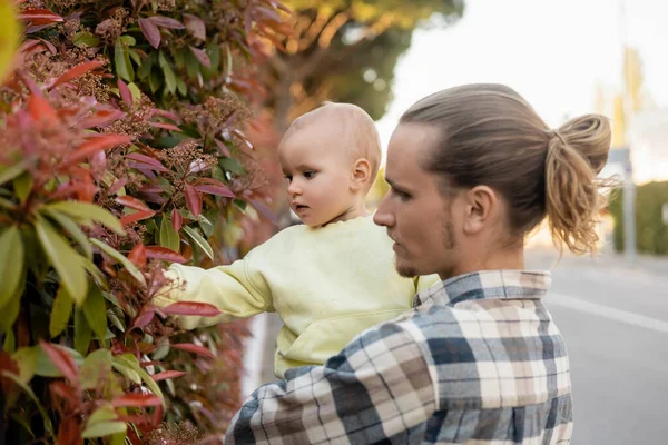 Мужчина держит маленькую дочь возле растения на открытом воздухе — стоковое фото
