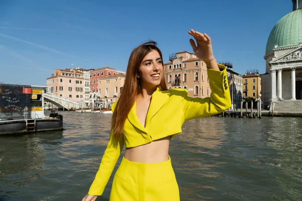 Mujer feliz en traje amarillo mirando lejos cerca del Gran Canal en Venecia - foto de stock
