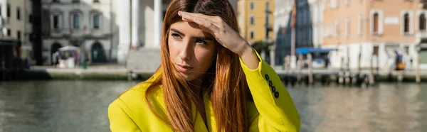 Молодая рыжая женщина держит руку над глазами и смотрит в сторону в Венеции, баннер — стоковое фото