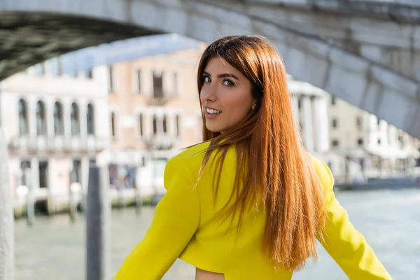 Heureuse rousse femme en veste de culture jaune souriant à la caméra sur fond flou à Venise — Photo de stock