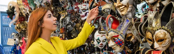 Amazed redhead woman choosing colorful carnival mask in Venice, banner — Stock Photo