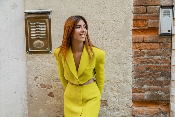 Mujer alegre en ropa amarilla mirando lejos cerca de la pared en la calle veneciana - foto de stock