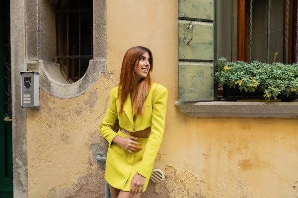 Fröhliche Frau im gelben Anzug, die in der Nähe eines Fensters mit Topfblumen in Venedig steht — Stockfoto