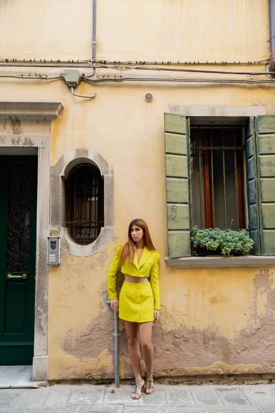 Jeune femme tendance en jaune debout près du bâtiment vénitien avec des fleurs sur la fenêtre — Photo de stock