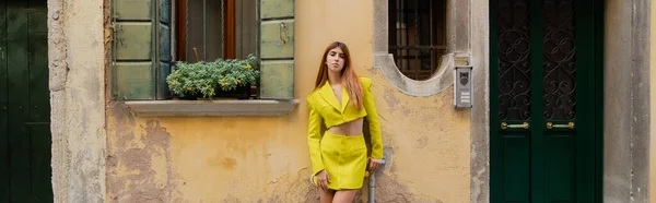 Молодая женщина в жёлтом костюме позирует возле горшечника с цветами на окне в Венеции, баннер — стоковое фото