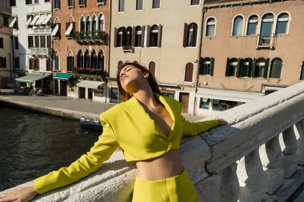 Frau im gelben Anzug entspannt mit geschlossenen Augen auf Brücke in Venedig — Stockfoto