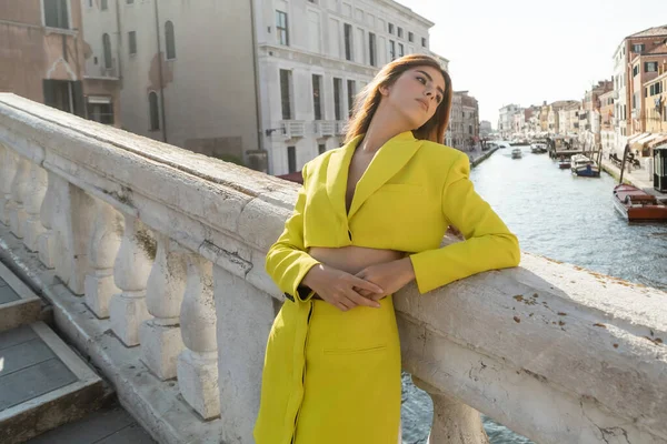 Молода жінка в жовтому костюмі спирається на балюстраду моста через Гранд-канал у Венеції. — стокове фото