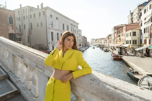 Young woman in yellow trendy clothes fixing red hair on bridge over Grand Canal in Venice — Stock Photo