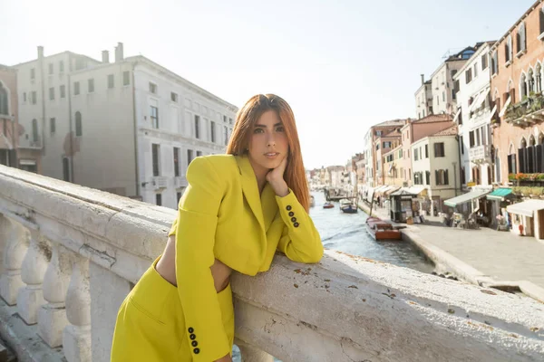 Trendy redhead woman looking at camera while standing on bridge over venetian Grand Canal — Stock Photo