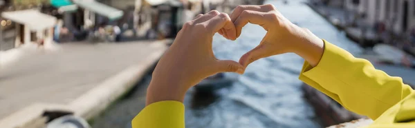 Vista recortada de la mujer que muestra el símbolo del corazón sobre fondo borroso en Venecia, bandera - foto de stock