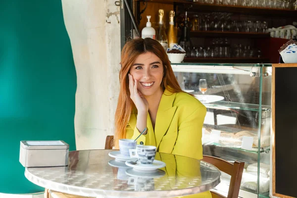 Happy woman in yellow jacket sitting near coffee cups on summer terrace in Venice — Stock Photo