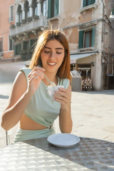 Smiling woman in elegant dress holding teaspoon and coffee cup on cafe terrace in Venice — Stock Photo