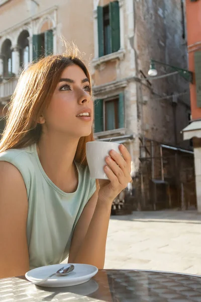 Redhead woman with coffee cup looking away on blurred venetian street — Stock Photo