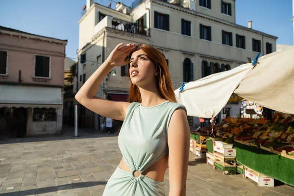 Elegante donna con mano sopra gli occhi guardando lontano sulla strada veneziana vicino al mercato alimentare — Foto stock