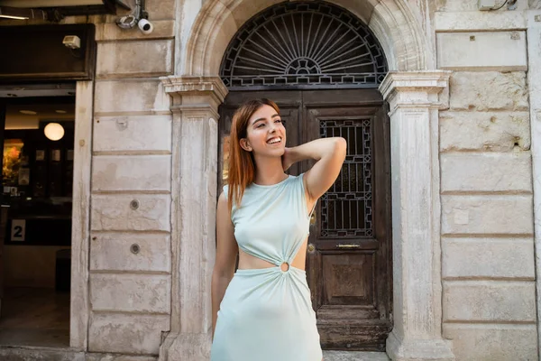 Glückliche Frau in elegantem Kleid, die auf der Straße in Venedig wegschaut und den Hals berührt — Stockfoto