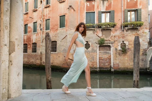 Piena lunghezza della donna alla moda con i capelli rossi a piedi lungo il canale sulla strada veneziana — Foto stock