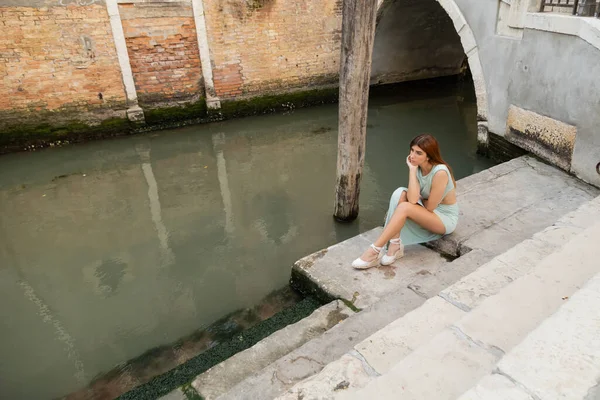 Elegante Frau sitzt in voller Länge auf einer Treppe in der Nähe eines Straßenkanals in Venedig — Stockfoto