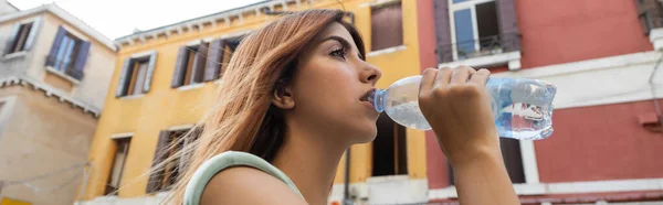 Vista de ángulo bajo de la pelirroja bebiendo agua refrescante en la calle en Venecia, pancarta - foto de stock