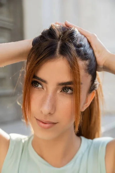 Close up portrait of young woman with freckles touching red hair and looking away outdoors — Stock Photo