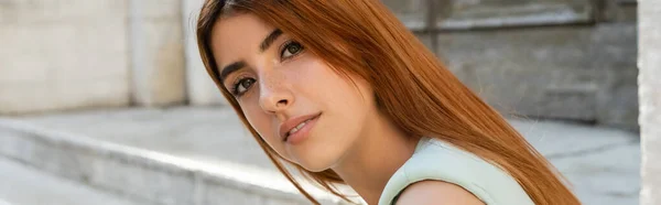 Joven mujer europea con el pelo rojo mirando a la cámara al aire libre, pancarta - foto de stock