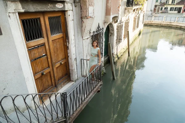 Femme en robe élégante debout sur le balcon du bâtiment médiéval sur le canal à Venise — Photo de stock