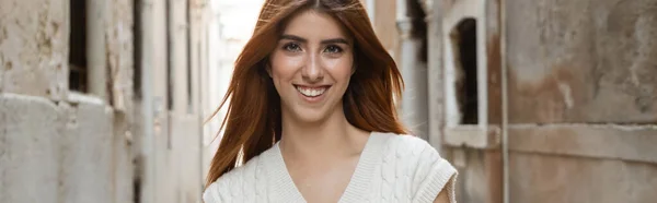 Charming woman with red hair smiling at camera on blurred lane in Venice, banner — Stock Photo