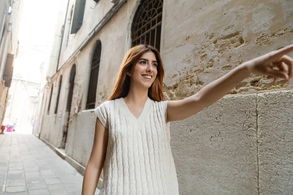 Donna allegra in maglione senza maniche che punta con il dito sulla strada veneziana — Foto stock