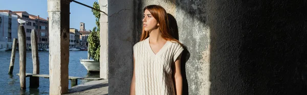 Молодая женщина в свитере без рукавов, смотрящая на Гранд-канал возле каменной стены в Венеции, баннер — стоковое фото