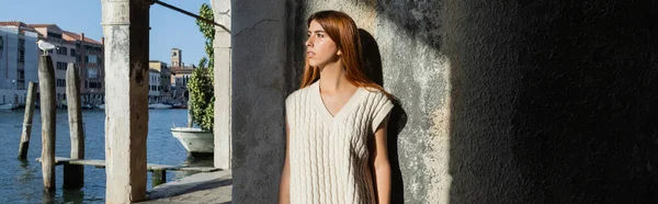 Giovane donna in maglione senza maniche guardando Canal Grande vicino al muro di pietra a Venezia, striscione — Foto stock