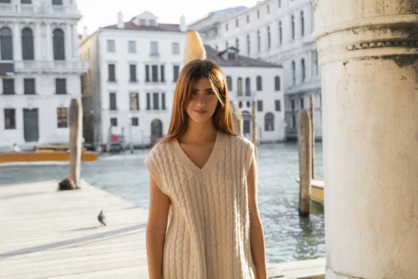 Руда жінка в безрукавичному стрибунці дивиться на камеру біля розмитого Гранд-каналу у Венеції. — Stock Photo