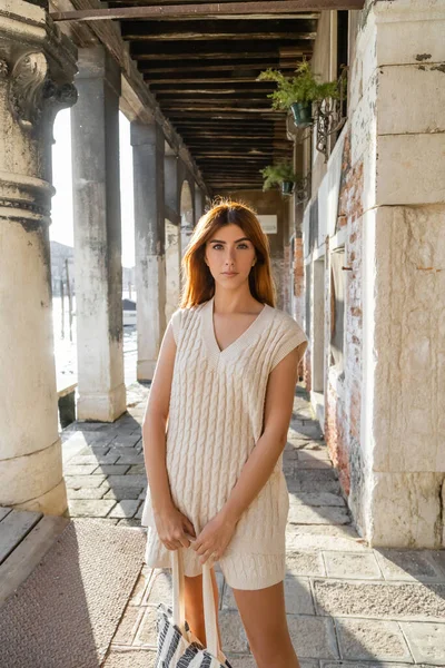 Redhead woman in sleeveless jumper looking at camera near colonnade in Venice — Stock Photo