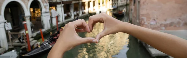 Vista parcial de la mujer que muestra el símbolo del corazón sobre fondo borroso en Venecia, bandera - foto de stock