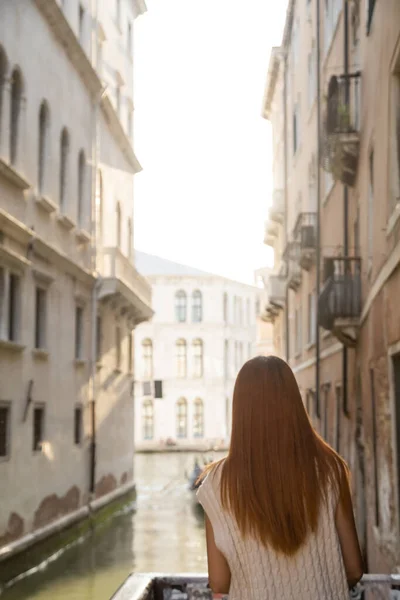 Rückansicht einer Frau mit roten Haaren in der Nähe verschwommener mittelalterlicher Gebäude in Venedig — Stockfoto